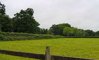 a grassy field with a wooden fence in the foreground and trees in the background at Woodhouse Woodmancote