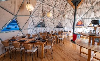 a restaurant with wooden tables and chairs , surrounded by a white geodesic dome , creating a unique and cozy atmosphere at Ecocamp Patagonia