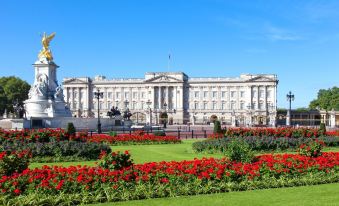 a large white building with a flag on top is surrounded by red flowers in a garden at The Kings Head Hotel