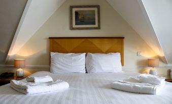 a white bed with a wooden headboard and two white towels on it , under a sloping ceiling at Grand Hotel Swanage