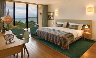 a hotel room with a king - sized bed , a desk , and a window overlooking the ocean at Martinhal Sagres Beach Family Resort Hotel