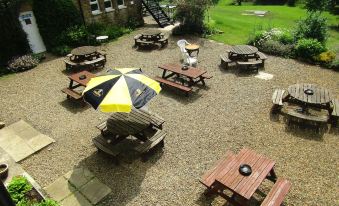 a large outdoor area with multiple picnic tables and benches , surrounded by grass and trees at The Twice Brewed Inn