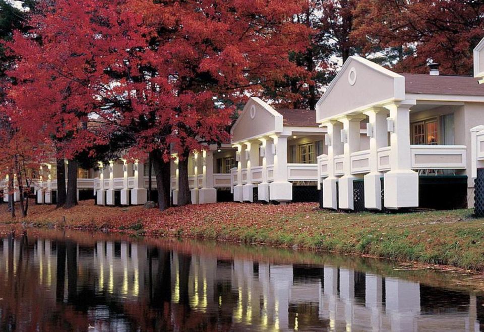 a serene scene of a lake with a row of white houses , reflecting in the water and trees in the background at Paradise Stream Resort