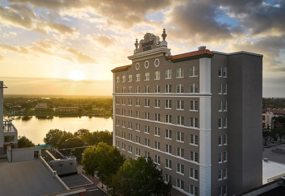 a large white building with a red roof and a clock on the side is surrounded by trees and a body of water at The Terrace Hotel Lakeland, Tapestry Collection by Hilton