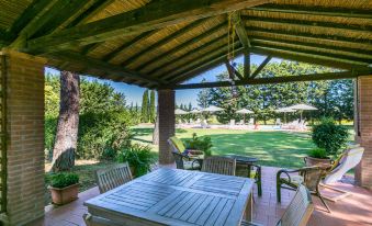 a wooden pergola with a dining table and chairs underneath it , overlooking a lush green lawn and a pool at Marrone