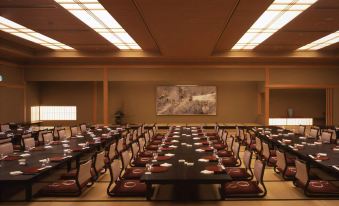 a large room with multiple tables set up for dining , surrounded by chairs and a screen at Imabari Kokusai Hotel