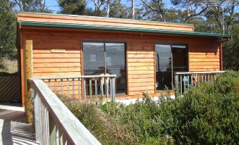 a wooden house with a green roof and large windows , situated on a hillside surrounded by trees at Bruny Island Escapes and Hotel Bruny