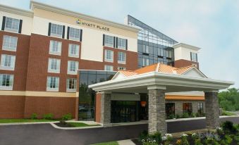 an exterior view of a hyatt place hotel , featuring a large brick building with a green lawn and a brick walkway leading up to the entrance at Hyatt Place Saratoga Malta