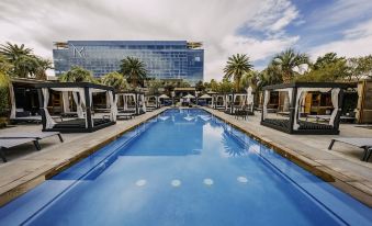 a large swimming pool surrounded by lounge chairs and palm trees , with a modern building in the background at M Resort Spa & Casino