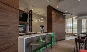 a modern bar area with a white and green bar , chairs , and a television mounted on the wall at Hilton Garden Inn Dallas - at Hurst Conference Center