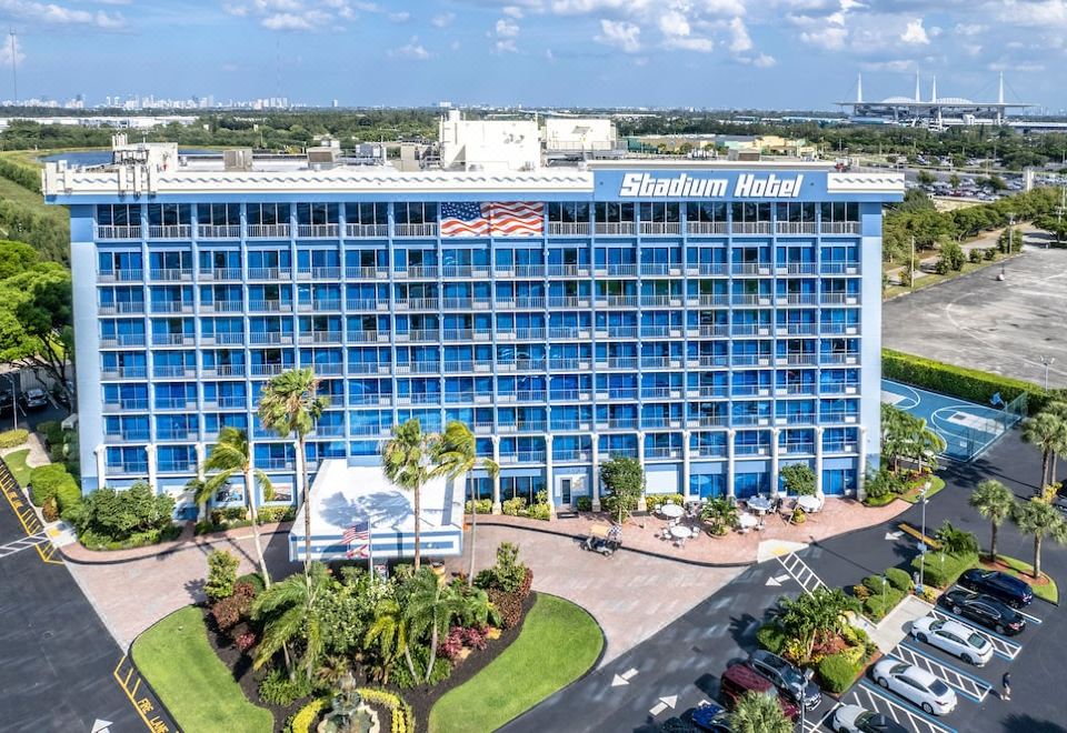 aerial view of a large hotel building with blue walls and a parking lot in front at Stadium Hotel