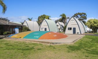 a group of small , colorful buildings surrounded by grass and trees , with a large tent - like structure in the background at Discovery Parks - Bunbury