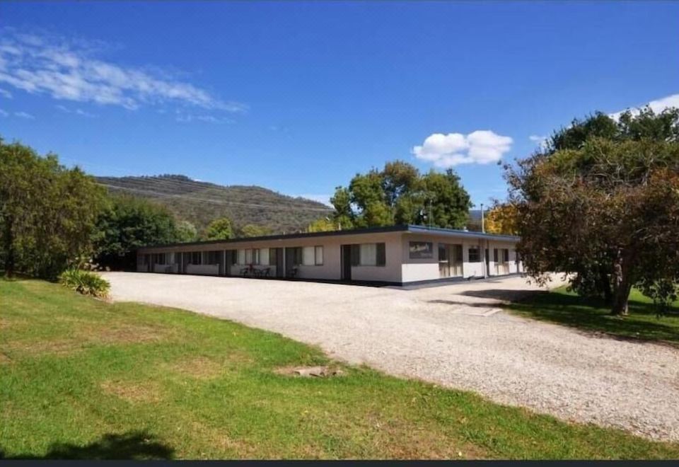 a large white building with a gravel driveway and green grass in front of it at Mount Beauty Motor Inn