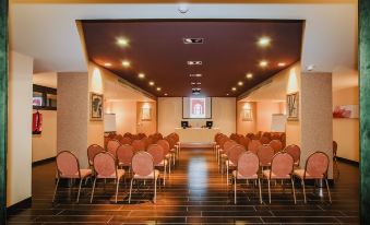 a large conference room with rows of chairs arranged in a semicircle , and a projector screen mounted on the wall at B Bou Hotel la Vinuela & Spa