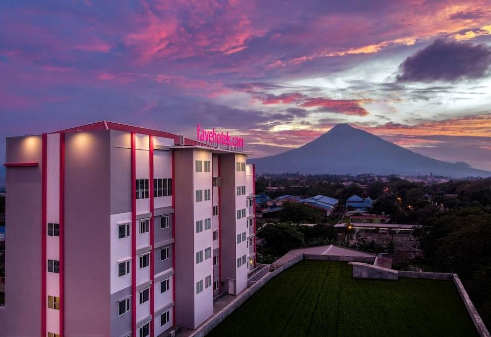 a tall building with a pink sign on the side is surrounded by greenery and a mountain in the background at favehotel Bitung