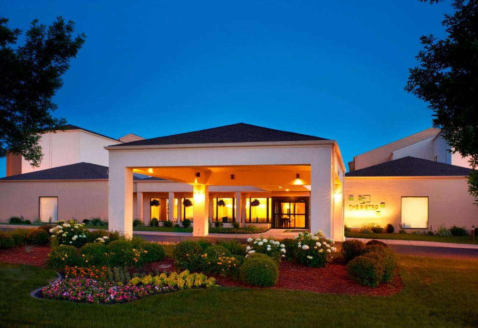 a hotel with a white exterior , lit up at night , surrounded by greenery and flowers at Courtyard Minneapolis-St. Paul Airport