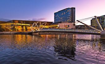 a large building with a tower is reflected in the water near a bridge and a bridge structure at Pan Pacific Melbourne