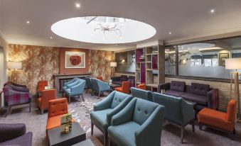 a modern lounge area with blue and orange chairs , a round light fixture , and a chandelier at Castle Green Hotel in Kendal, BW Premier Collection