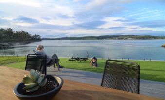 a woman sitting on a bench near a lake , enjoying the view from a patio at Eastcoaster Tasmania