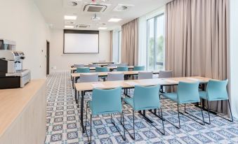 a conference room with blue chairs and tables , a projector screen , and large windows at Hampton by Hilton Oswiecim
