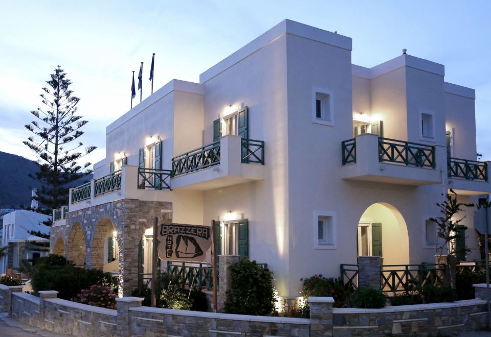 A large white building with balconies and illuminated lights on its side during dusk or nighttime at Brazzera Hotel