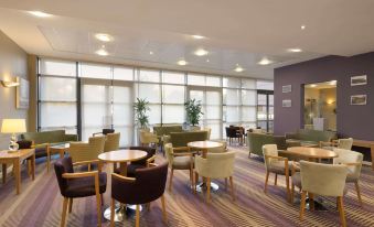 a modern lounge area with multiple couches , chairs , and tables arranged in an open space at Ramada Plaza by Wyndham Wrexham