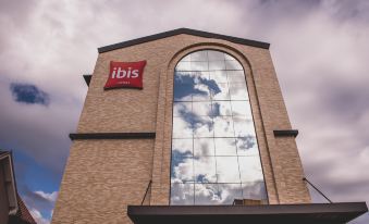 a brick building with a large window and an ibis sign on the side , reflecting the sky at Ibis Carlos Barbosa