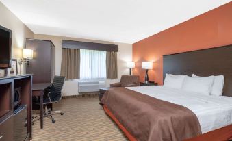 a hotel room with a large bed , a desk , and various items on the desk at AmericInn by Wyndham Rogers