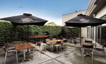 an outdoor patio area with multiple tables and chairs , umbrellas , and greenery , under a clear blue sky at Nightcap at Gateway Hotel
