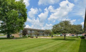 a large building surrounded by a grassy field , with a group of people standing in front of it at SureStay Hotel by Best Western Bowling Green North