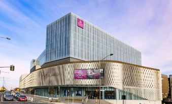 a large building with a pink sign on top and people walking in front of it at Sage Melbourne Ringwood