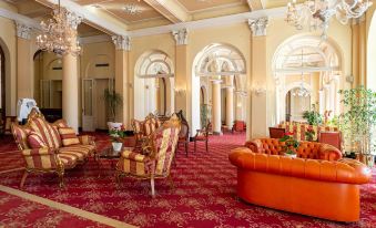 a luxurious hotel lobby with a red carpeted floor , multiple chairs , and a large couch at Grand Hotel Cadenabbia