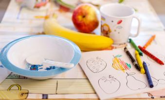 a table with a blue bowl , a mug , and a coloring page of fruit on it at Hotel Geneva by Fassbind