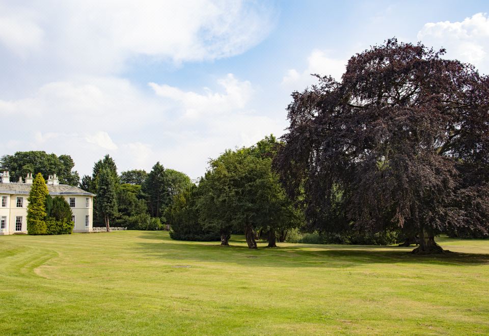 a large open field with trees and a white house in the background , under a partly cloudy sky at Eastwood Hall