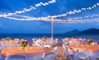 a beach wedding reception with white tables and chairs under a string of lights , set up on the sand at St. Kitts Marriott Resort & the Royal Beach Casino