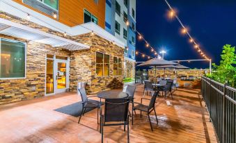 a patio with a dining table and chairs , surrounded by a brick wall and lit by string lights at Fairfield Inn & Suites Houston League City