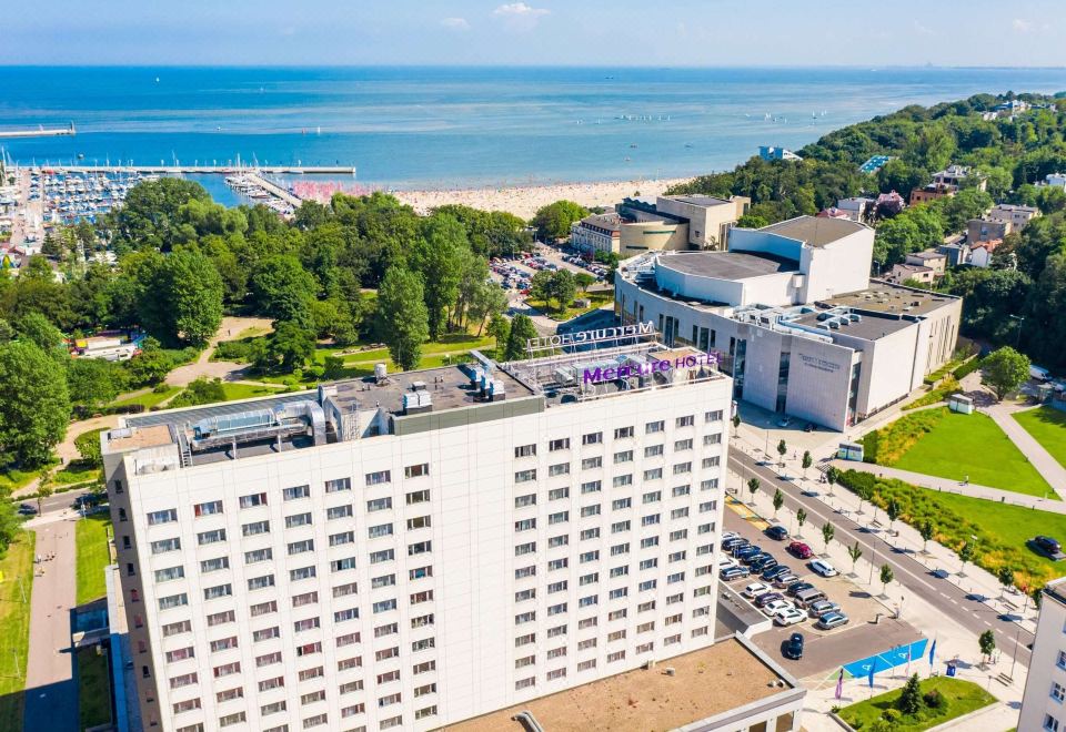 aerial view of a large white building surrounded by trees and a body of water at Hotel Mercure Gdynia Centrum