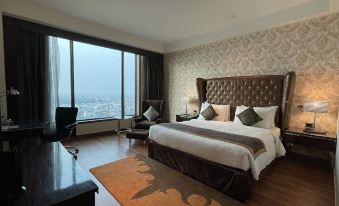 a large bed with a tufted headboard is in the middle of a room with a window and a rug at Radisson Blu Hotel New Delhi Paschim Vihar