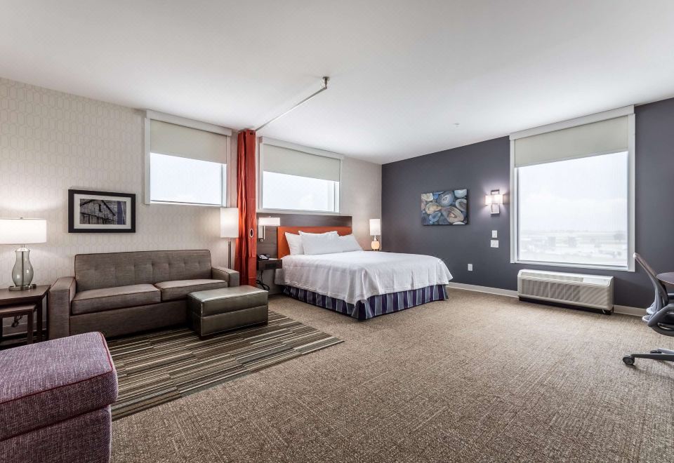 a modern hotel room with a large bed , couch , and television , as well as a view of the city through a window at Home2 Suites by Hilton Fort Worth  Northlake