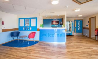 a modern office reception area with blue walls , wooden floors , and a wooden desk equipped with a computer at Travelodge Stafford M6