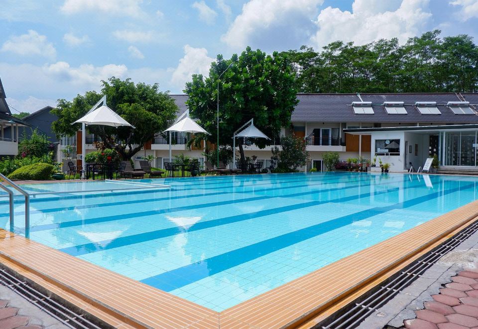 a large outdoor swimming pool surrounded by grass , trees , and umbrellas , with people enjoying their time in the pool area at Front One Resort Magelang