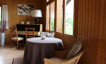 a cozy wooden room with a round table and chairs , large windows , and a piano at Hotel Roc et Neige