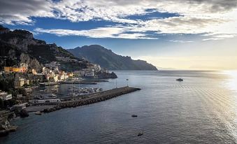 a beautiful coastal town with boats in the water and mountains in the background , under a cloudy sky at Hotel Miramalfi