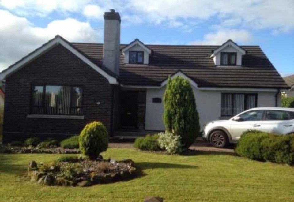 a large white house surrounded by a lush green lawn , with a car parked in front of it at Tara House