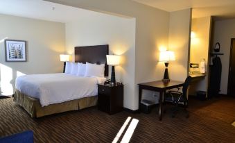 a hotel room with a king - sized bed , a desk , and a bathroom in the background at Cobblestone Inn & Suites - Holstein