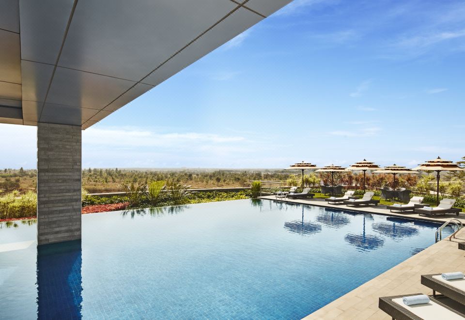 a large swimming pool is seen from a high vantage point , with lounge chairs and umbrellas around it at Taj Bangalore