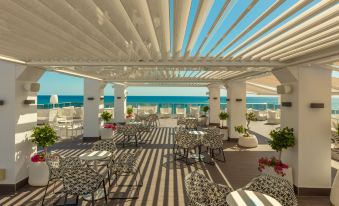 a modern , open - air terrace with white pergolas and black - and - white striped tables , overlooking the ocean and palm trees under at RH Bayren Hotel & Spa