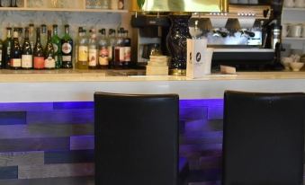 a well - equipped bar with several bottles and wine glasses on display , along with a sink and two stools at Le Cheval Blanc - Logis Hotel