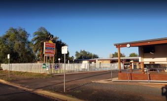 a motel with a large sign and a white fence in front of a brown building at Copper City Motel