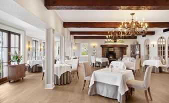 a large dining room with wooden floors , white tablecloths on the tables , and a chandelier hanging from the ceiling at Manoir Hovey